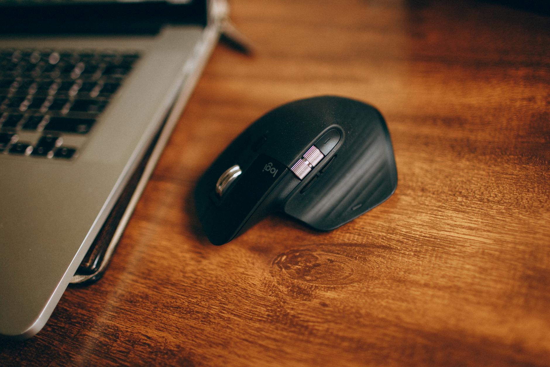 Bezprzewodowa mysz obok laptopa na drewnianym biurku