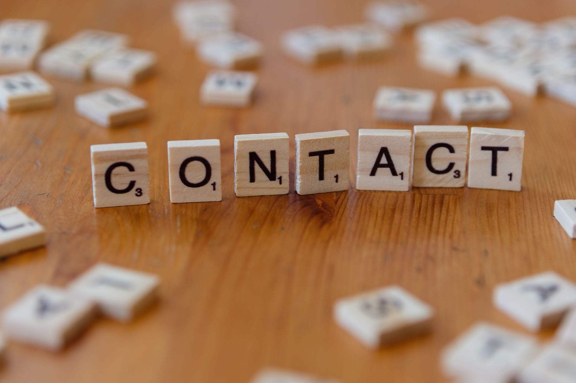 Litery Scrabble układające słowo contact na drewnianym stole