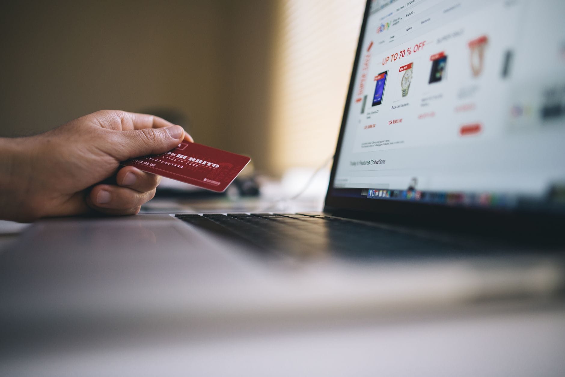 Osoba trzymająca kartę płatniczą przed laptopem podczas zakupów online Osoba trzymająca kartę płatniczą przed laptopem podczas zakupów online